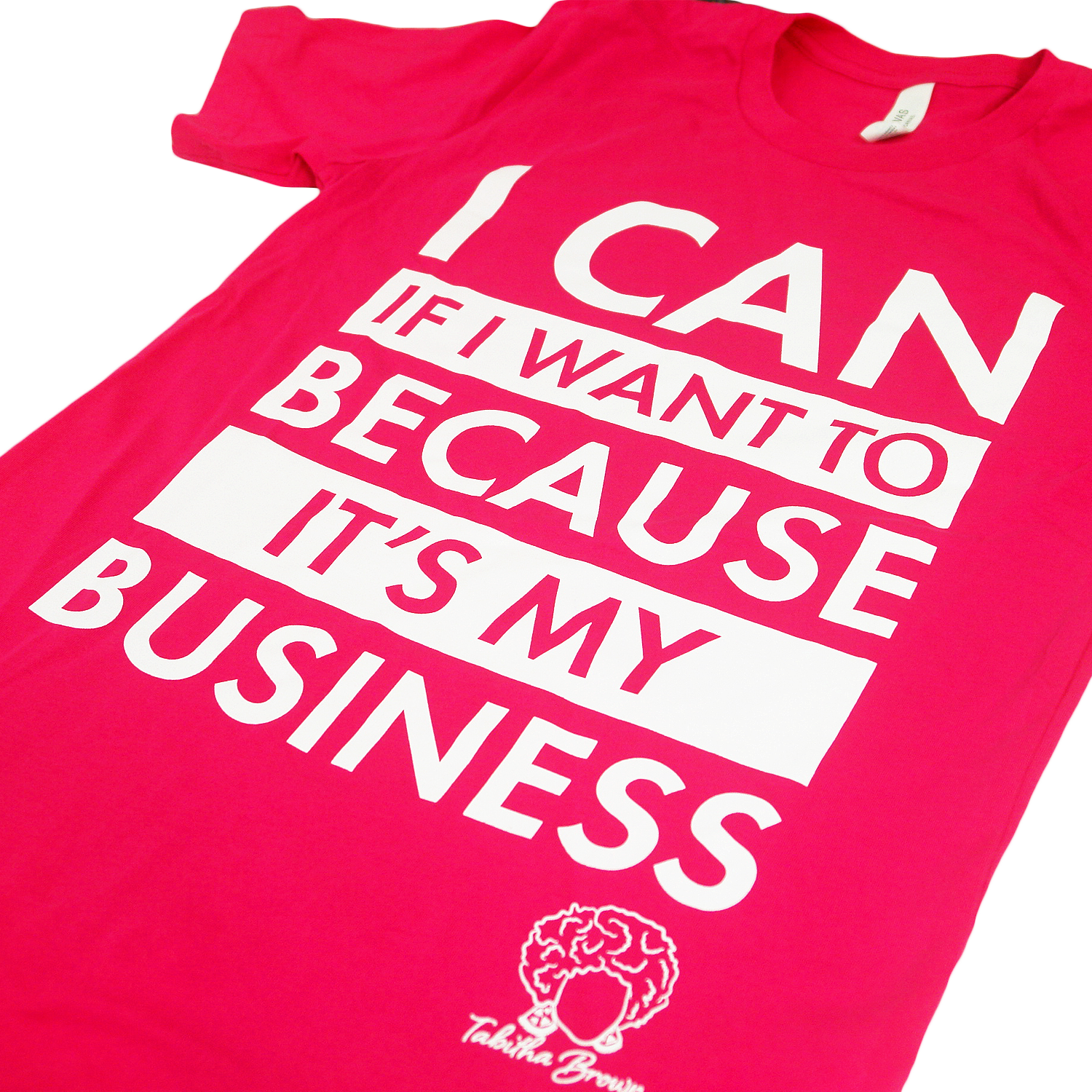 close up angled photo of image of heliconia tee shirt on clear background. full chest print in white that is stacked and reads "i can if i want to because it's my business" with tabitha brown's logo of her head with earrings and her name in cursive below on the right.