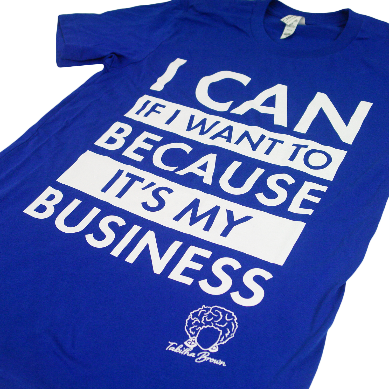 close up angled photo of image of royal blue tee shirt on clear background. full chest print in white that is stacked and reads "i can if i want to because it's my business" with tabitha brown's logo of her head with earrings and her name in cursive below on the right.
